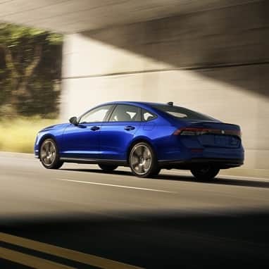 2026 Honda Accord in Still Night Pearl, rear 3/4 view, driving out from under the overpass.